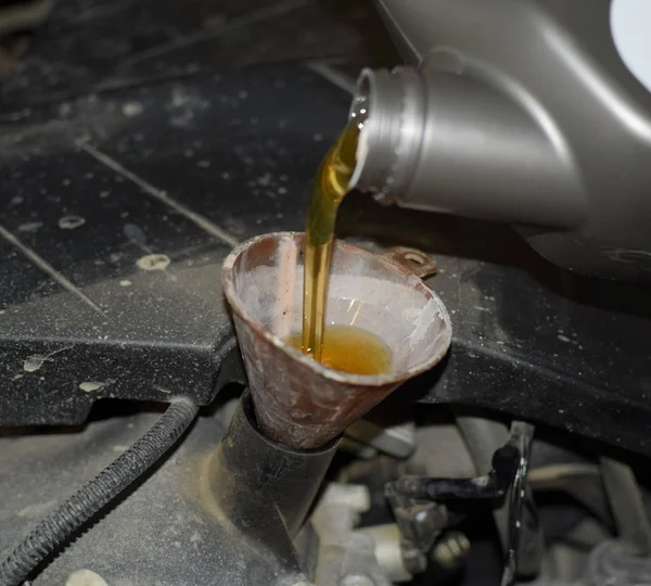 Oil change in the engine of the car. Filling the oil through the funnel. Car maintenance station.
