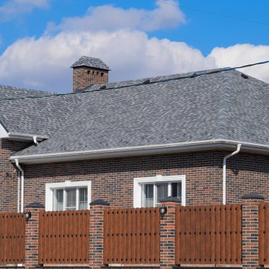 Asfalt shingle. Dekoratif bitüm Zona bir tuğla ev çatısında. Oluklu metal çit yapılmış.