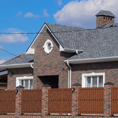 Asfalt shingle. Dekoratif bitüm Zona bir tuğla ev çatısında. Oluklu metal çit yapılmış.