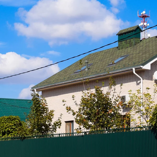 Asphalt shingle. Decorative bitumen shingles on the roof of a brick house. Fence made of corrugated metal.