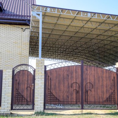 Bir çit ve gates ile tuğla ev. Çelik çerçeve ile büyük bir tente. Görünümü yeni bir İnşaatlı çit ve tuğla ve oluklu metal yapılmış bir ev.