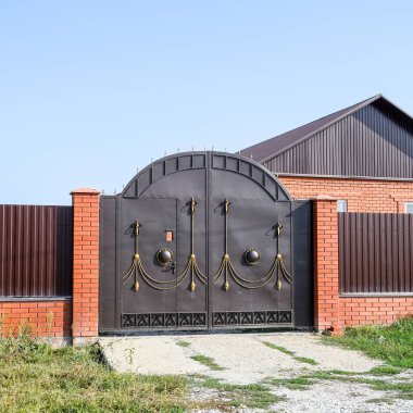 Bir çit ve gates ile tuğla ev. Görünümü yeni bir İnşaatlı çit ve tuğla ve oluklu metal yapılmış bir ev.