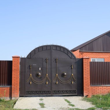 Bir çit ve gates ile tuğla ev. Görünümü yeni bir İnşaatlı çit ve tuğla ve oluklu metal yapılmış bir ev.