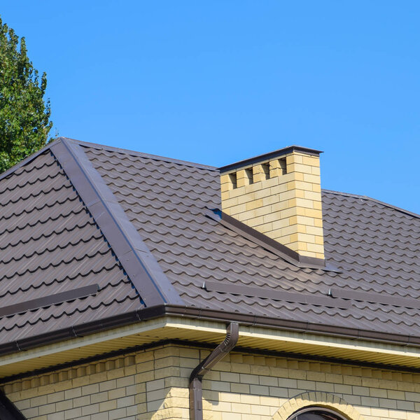 Brown corrugated metal profile roof. Chimney and ventilation of yellow brick.
