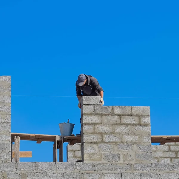Stavitel staví zdi domu ze škvárové bloku. Dělník na stavbě. — Stock fotografie