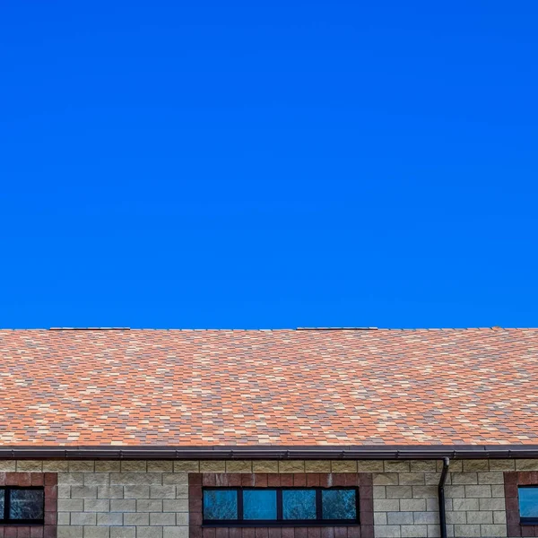La casa está hecha de ladrillos beige, el techo está cubierto con tejas de betún. Ventanas metálicas de plástico en la casa . — Foto de Stock