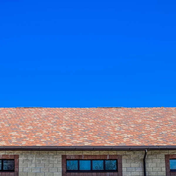 La casa está hecha de ladrillos beige, el techo está cubierto con tejas de betún. Ventanas metálicas de plástico en la casa . —  Fotos de Stock