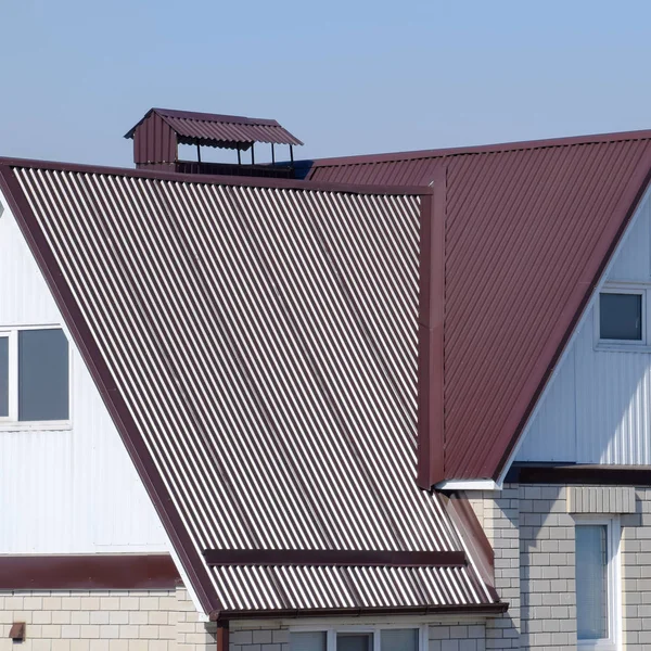 La casa es con un ático y un techo combinado. Casa con ventanas de plástico y un techo marrón de chapa corrugada —  Fotos de Stock