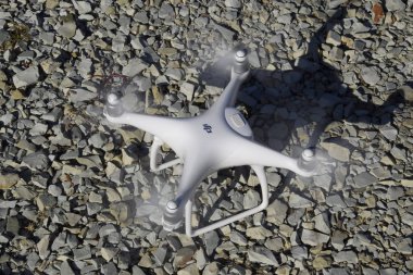 Drone Phantom 4 çakıl üzerinde duruyor ve pervaneleri döner. Drone uçuşunda hazırlık.