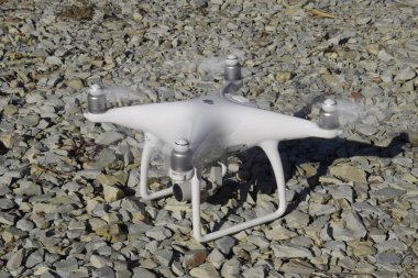 Drone Phantom 4 çakıl üzerinde duruyor ve pervaneleri döner. Drone uçuşunda hazırlık.