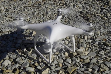 Drone Phantom 4 çakıl üzerinde duruyor ve pervaneleri döner. Drone uçuşunda hazırlık.