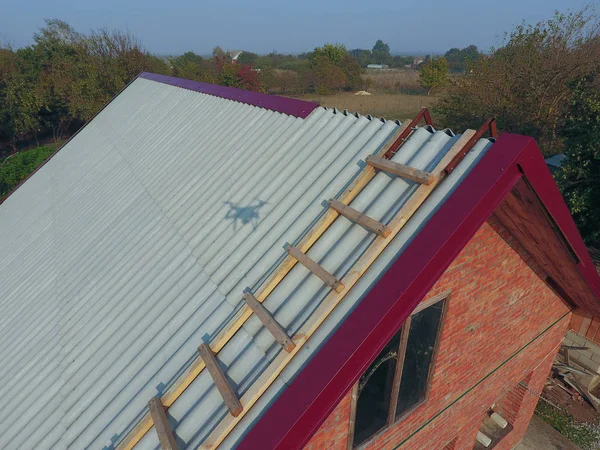 Construção de telhado da casa, uma escada de madeira para o telhado com um gancho, os cantos dos patins do perfil de metal vermelho . — Fotografia de Stock