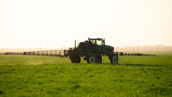 Traktor im Hintergrund des Sonnenuntergangs. Traktor mit hohen Rädern macht Dünger auf jungen Weizen. — Stockfoto