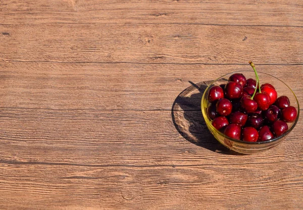 Berries of a sweet cherry in a glass bowl on a wooden background. Ripe red sweet cherry