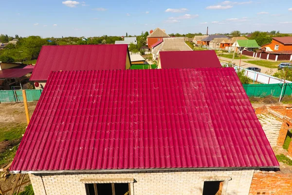 Dům s červenou střechou vyrobené z vlnitého plechu. Střecha z vlnitého kovového profilu. Kovová taška na střechu. — Stock fotografie