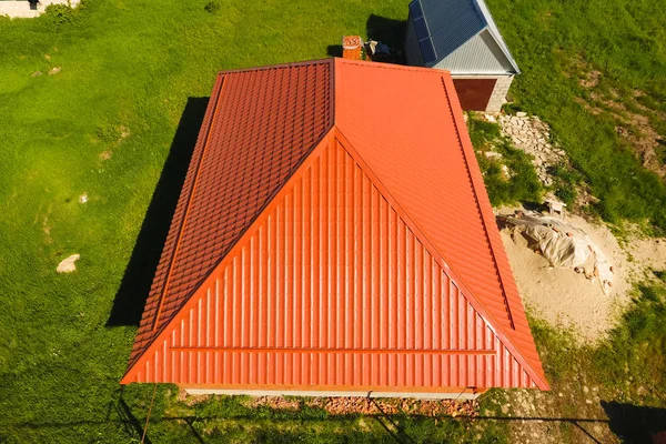 House with an orange roof made of metal, top view. Metallic profile painted corrugated on the roof.