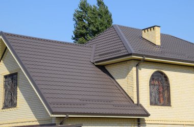 Sarı tuğla ve kahverengi oluklu çatı evi metalden yapılmış. Windows kafesler.