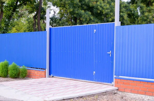 Fence and gate from sheets of blue corrugated metal.