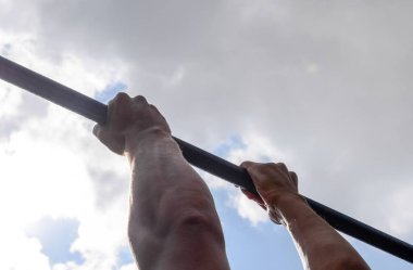 Çubuğunda eller yakın çekim. Adam kendini çubuğunda çeker. Temiz havada spor oynarken. Yatay çubuk.