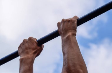 Çubuğunda eller yakın çekim. Adam kendini çubuğunda çeker. Temiz havada spor oynarken. Yatay çubuk.