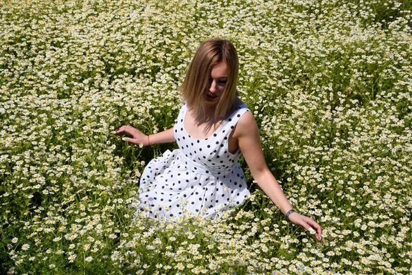 Eine Frau im weißen Kleid mit Tupfen steht auf einer Lichtung mit Gänseblümchen. Blühende Margeriten — Stockfoto