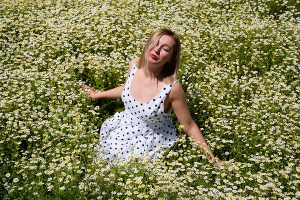 En kvinna i en vit klänning med prickar är på en gläntan med prästkragar. Blommande prästkragar — Stockfoto