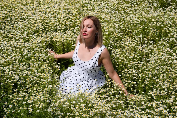 Uma mulher em um vestido branco com bolinhas está em uma clareira com margaridas. Margaridas em flor — Fotografia de Stock