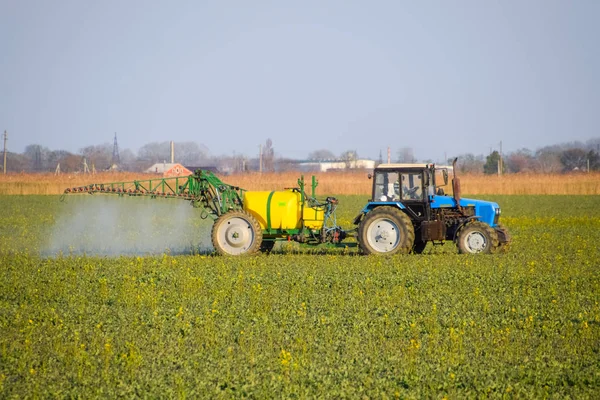 Traktor termékenyít egy Kanola területén, permetezés műtrágya a traktor. — Stock Fotó