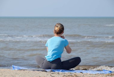 kız deniz kenarında yoga uygular. Deniz tarafından temiz havada egzersiz jimnastik.