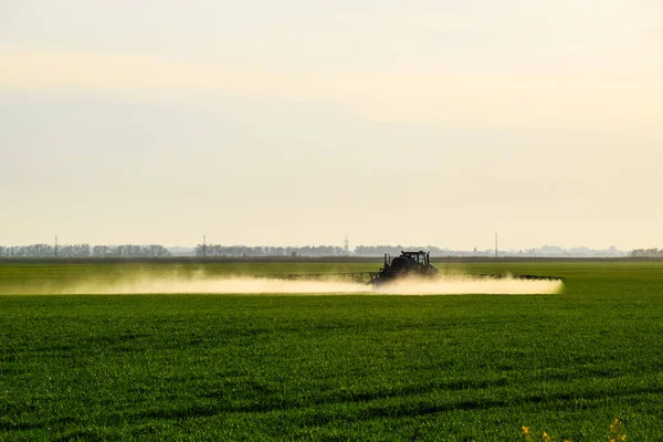 Traktor s pomocí postřikovače rozstřikuje tekutá hnojiva na mladou pšenici na poli. — Stock fotografie