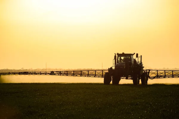 Traktor s pomocí postřikovače rozstřikuje tekutá hnojiva na mladou pšenici na poli. — Stock fotografie