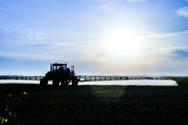 Traktor s pomocí postřikovače rozstřikuje tekutá hnojiva na mladou pšenici na poli. — Stock fotografie