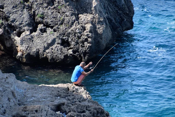 Pescador con caña de pescar en una roca junto al mar Mediterráneo . —  Fotos de Stock