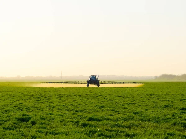 Traktor na slunce pozadí. Traktor s vysoká kola dělá hnojivo na mladé pšenice. Používání chemických látek jemně dispergované sprej — Stock fotografie