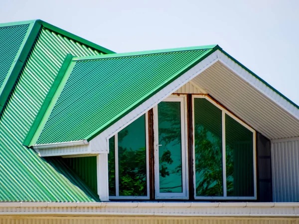 The house with plastic windows and a green roof of corrugated sheet. Green roof of corrugated metal profile and plastic windows.