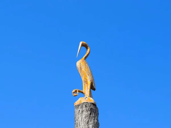 Kranich-Figur auf Baumstumpf gegen den blauen Himmel. Tierfiguren aus Holz. Holzschnitzerei — Stockfoto