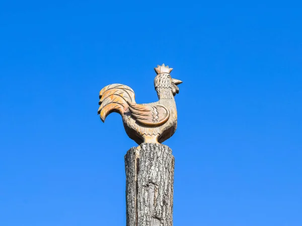 Figura, a kakas a egy fatönkön, háttérben a kék ég. Fából készült számok az állatok. Fafaragó — Stock Fotó