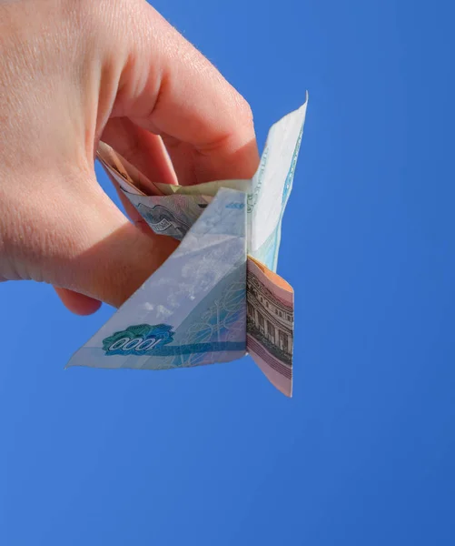 Denominations of Russian money, folded in the airplane against the blue sky in hand
