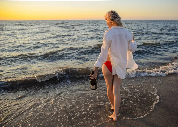 Junges Mädchen am Strand mit einer Flasche Champagner und einem Glas, Frau ging ins Wasser am Strand. — Stockfoto