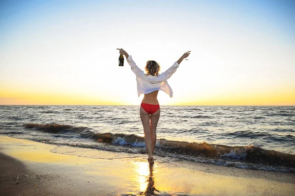 Junges Mädchen am Strand mit einer Flasche Champagner und einem Glas — Stockfoto