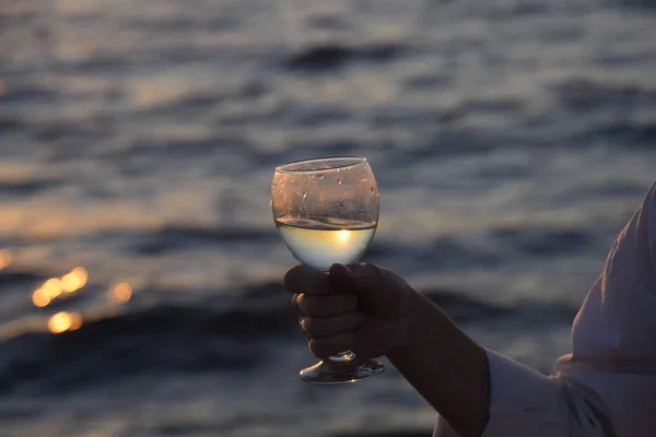 Copo de champanhe nas mãos de uma mulher na praia em um fundo pôr do sol . — Fotografia de Stock