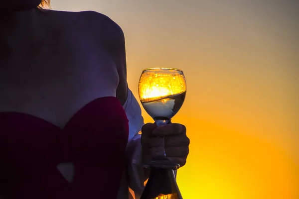 Copo de champanhe nas mãos de uma mulher na praia em um fundo pôr do sol . — Fotografia de Stock