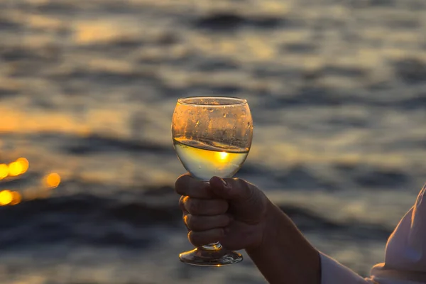Copo de champanhe nas mãos de uma mulher na praia em um fundo pôr do sol . — Fotografia de Stock