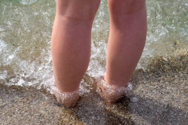 Deniz suyu ve kum karaya kadın bacaklar.