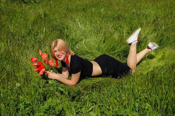女の子はチューリップの花束を持つ野原の草の上に横たわっている. — ストック写真