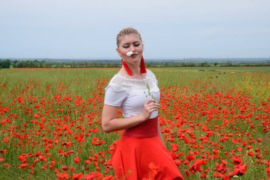 Kırmızı haşhaş tarlasının ortasında bir kızın ellerinde beyaz haşhaş çiçeği