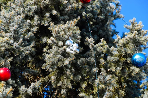 Decorations New Year tree. Tinsel and toys, balls and other decorations on the Christmas Christmas tree standing in the open air. — Stock Photo, Image