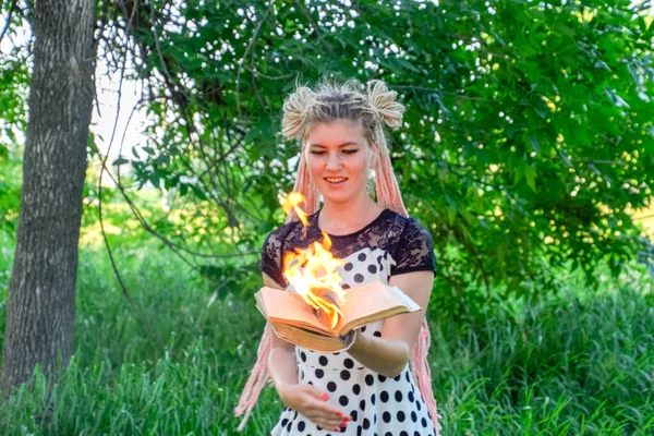 Девочка держит в руках горящую книгу. Молодая женщина в лесу сжигает книгу . — стоковое фото