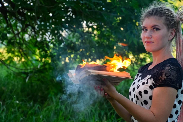 女孩手里拿着一本火热的书。 森林里的一个年轻女子把一本书烧掉了. — 图库照片