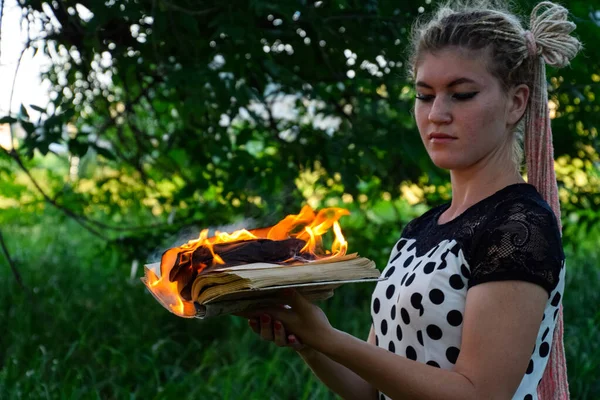 女孩手里拿着一本火热的书。 森林里的一个年轻女子把一本书烧掉了. — 图库照片